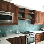 A kitchen with brown cabinets, white countertops, and a wall with scale cement tile