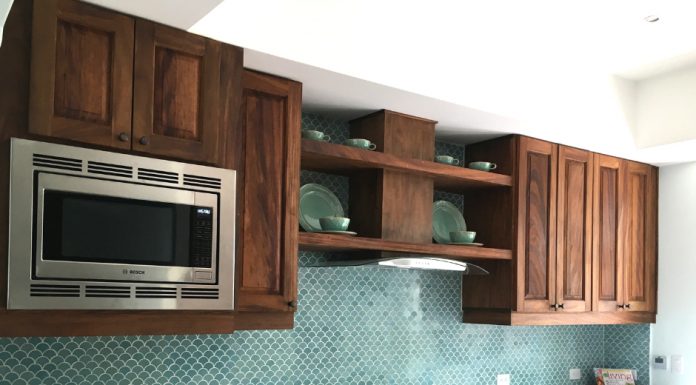 A kitchen with brown cabinets, white countertops, and a wall with scale cement tile